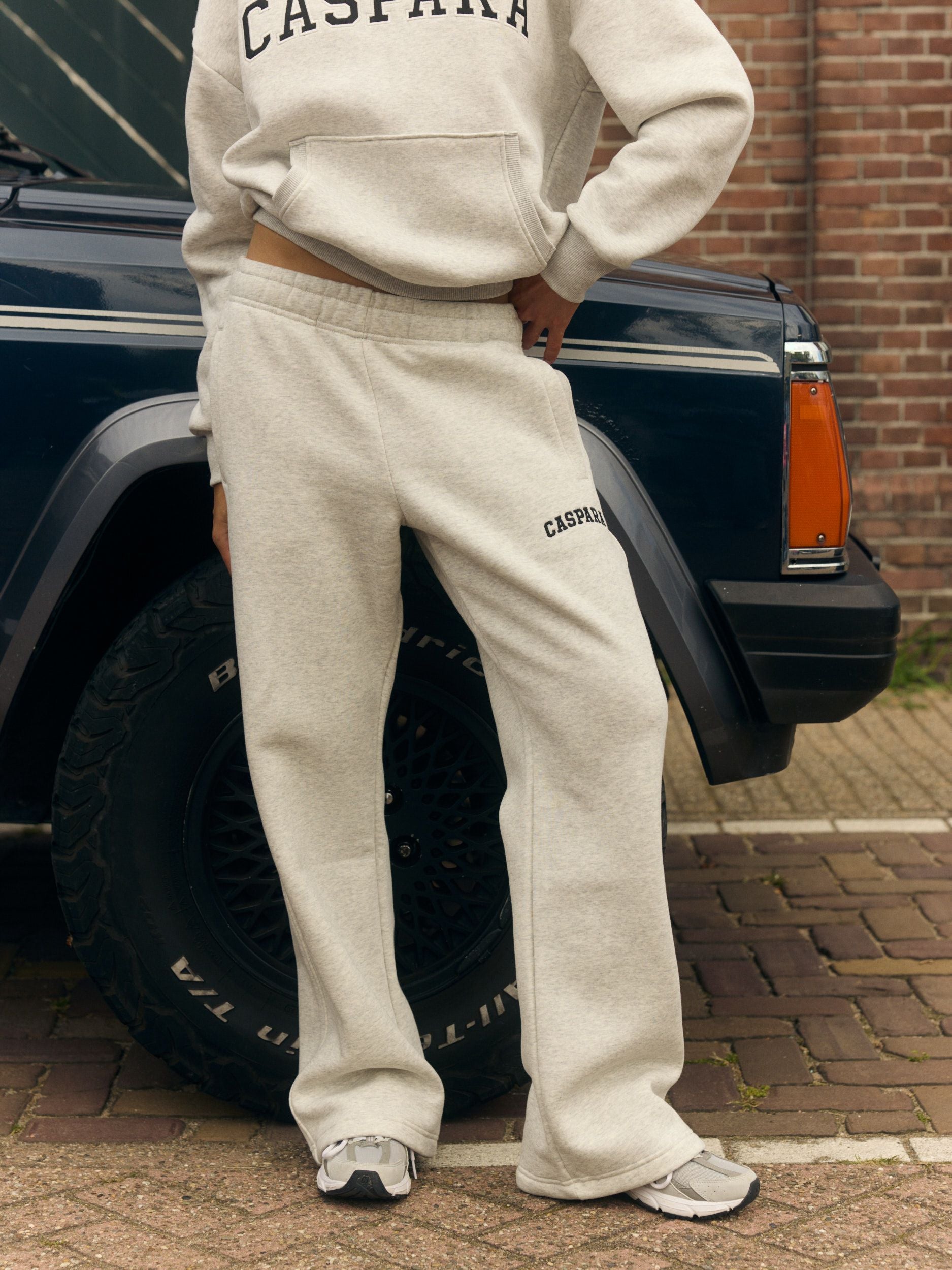 Woman wearing grey melange straight-leg sweatpants and a matching hoodie beside a vintage car.